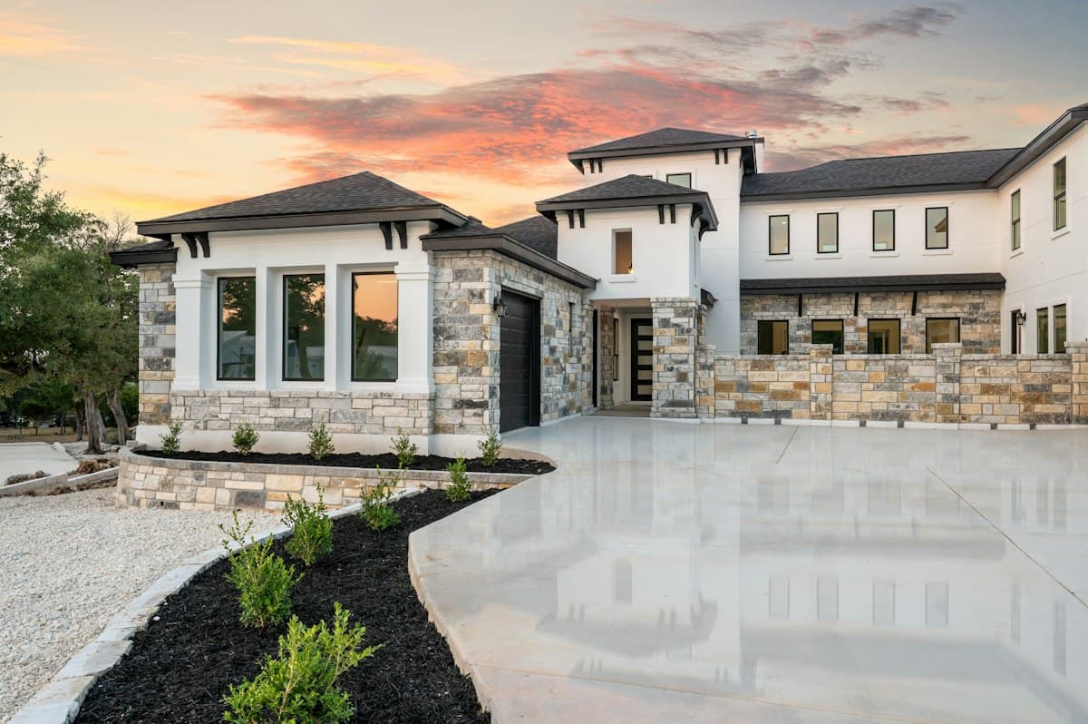 Modern stone-accented house at sunset with a long driveway